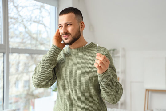 Young man feeling discomfort while cleaning ears with cotton buds at home