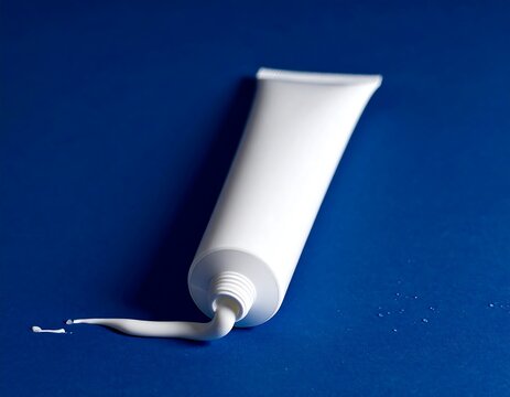 A white toothpaste tube lies on its side with toothpaste squeezed out on a blue surface.