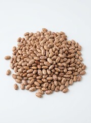 Fototapeta premium A pile of pinto beans rests on a white surface. The beans are a mix of light and dark brown colors with speckled patterns.