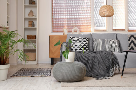 Interior of modern room with sofa, knitted plaid and pouf