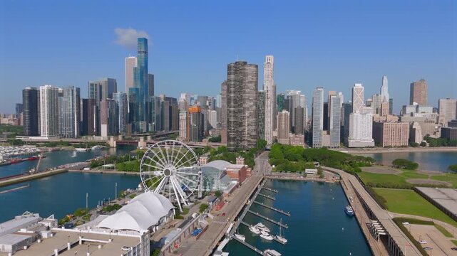 Stunning aerial footage captures Chicago Illinois downtown skyline featuring iconic ferris wheel at Navy Pier with marina and boats docked below, modern glass skyscrapers rising against clear blue sky
