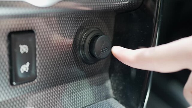 Pressing car cigarette lighter button close-up in vehicle interior 12V power socket