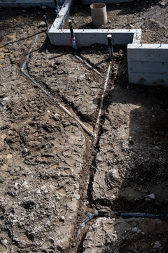View from above of pipes installed in dirt trenches in foundation of new home build, concrete foundation walls poured, construction work site
