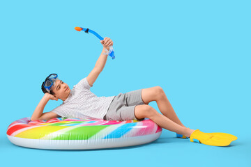 Cute little happy boy with inflatable mattress, snorkeling mask and flippers on blue background © Pixel-Shot