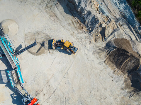 Aerial view of a yellow front loader moving gravel near a blue crushing machine at a construction site with piles of sand and dirt Indianapolis, Indiana, United States.