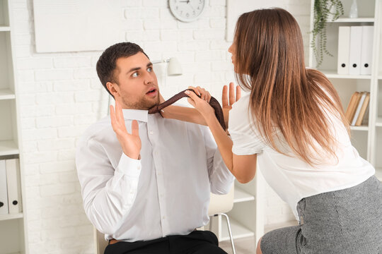 Business woman pulling her male colleague by his necktie in office. Harassment concept