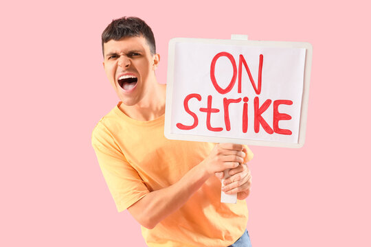 Protesting young man holding placard with text ON STRIKE against pink background