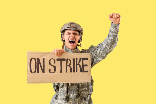 Protesting male soldier holding placard with text ON STRIKE against yellow background