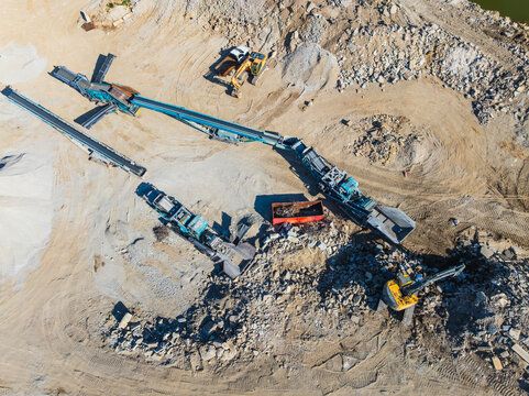 Aerial view of heavy machinery processing stone and gravel at an industrial quarry site with trucks and piles of earth in Indianapolis, Indiana, United States.