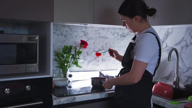 Woman cooks in bright, modern kitchen. Red rose adds romantic touch to scene. She handles food with care and focus. Perfect for love, home, or cooking themes. Kitchen features sleek marble backsplash
