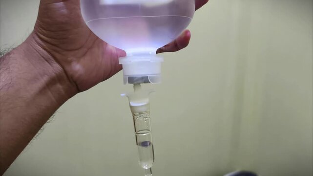 Close up of a hand holding an IV drip bag with fluid dripping.