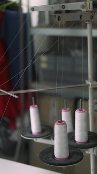 Vertical video. Thread spool factory. Textile studio equipment. White string unwound from bobbin sewing process in tailoring workplace.