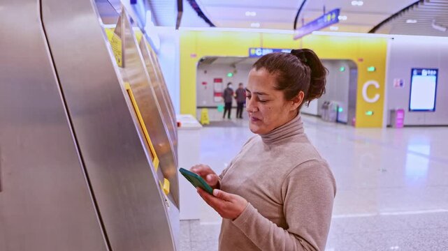 Smiling woman using smartphone to buy a subway ticket