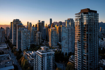 Fototapeta premium An enchanting dusk city landscape captures tall buildings illuminated against the darkening sky, surrounded by mountains, creating a perfect blend of natural and urban elements.