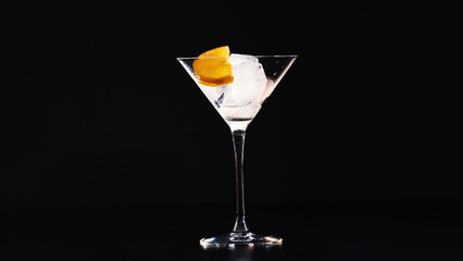Fototapeta premium Empty cocktail glass filled with ice and orange garnish against black
