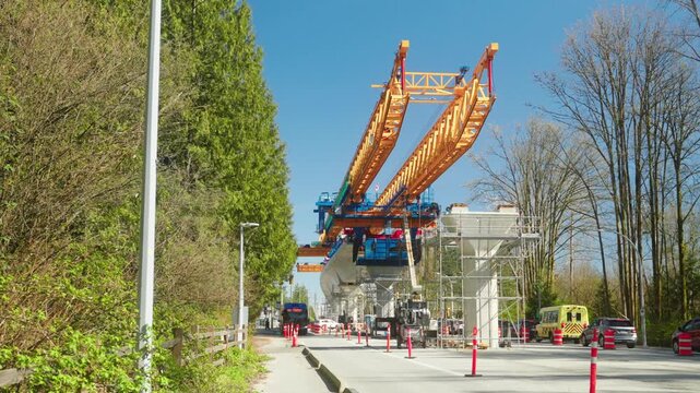 approaching wide angle perspective shows the massive yellow segment launcher extending over road to construct the elevated concrete transit guideway for the Surrey Langley SkyTrain extension under