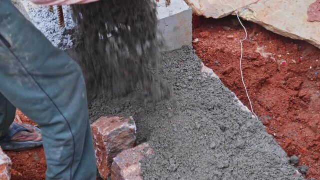 Worker pouring cement mortar on top of granite stones for basement construction at building site, hyderabad, telangana, india. day time, stable shot, 4k.