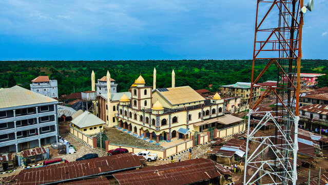 Aerial view of a mosque with yellow domes and minarets surrounded by urban buildings and a telecommunications tower in Igbaja, Kwara, Nigeria.