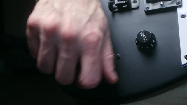 Close up guitarist hand adjusting pickup selector, turning volume knob on modern matte black electric guitar before playing, preparing for performance or practice session. 