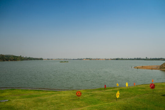 Lake with green lawn and flower wind spinner with blue sky background for peple to relax at large reservoir.