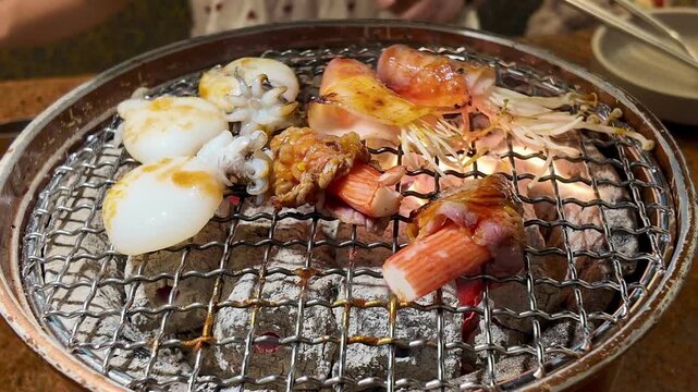 Fresh seafood and bacon wrapped enoki mushrooms grilling on a charcoal stove. popular grill style dining and dinner atmosphere