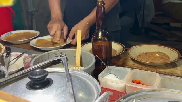 Traditional Indonesian street food scene showing a vendor manually grinding ingredients with a mortar and pestle to prepare ketoprak, a popular dish from Indonesia made of rice cakes (lontong).