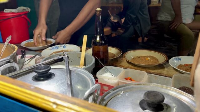 Traditional Indonesian street food scene showing a vendor manually grinding ingredients with a mortar and pestle to prepare ketoprak, a popular dish from Indonesia made of rice cakes (lontong).