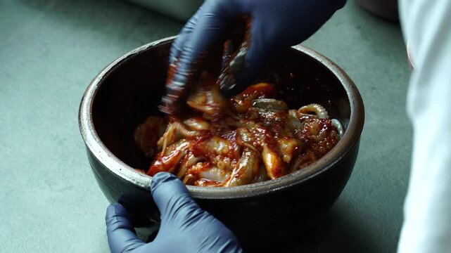 Mix raw squid with spicy seasoning in a glass bowl.