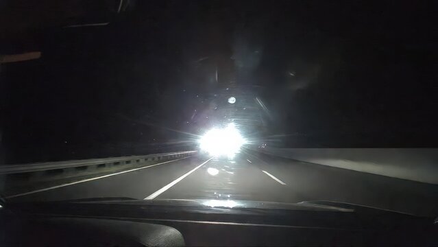 Dramatic road safety concept showing a driver struggling with intense oncoming headlights at night. Bright high-beam glare reduces visibility and creates a dangerous driving situation. Visual represen