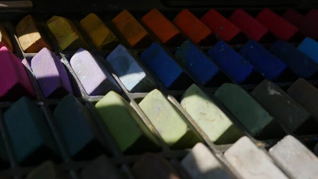 Colorful soft pastel chalk sticks arranged in a worn artist's palette box, vibrant rainbow art supply collection