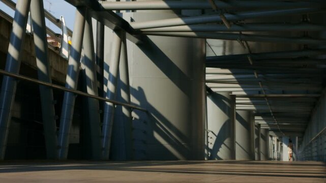 Dramatic perspective of an elevated walkway with steel tube roof structure casting striped shadows in golden morning light