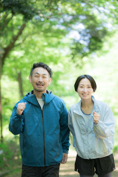新緑の公園でウォーキングやランニングのスポーツが楽しいミドル夫婦の正面カメラ目線笑顔　ダイエットや健康などの明るいイメージ