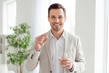 Fototapeta premium Smiling handsome man holding a vitamin pill and a glass of water for his health