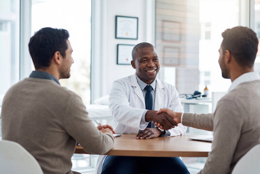 Friendly black doctor shaking hands with a patient in a medical office