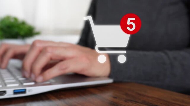 Close-up of a woman's hand working on a computer while pointing to a shopping cart animation with a notification of the number of items added.