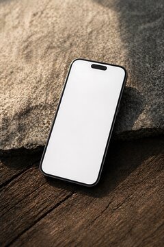 A modern smartphone with a blank white screen rests on a textured wooden surface next to a large, rough stone.