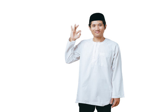 Young Muslim man in white baju kurung and black peci showing OK hand gesture with a confident smile against white background