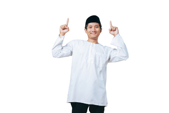 Happy young Muslim man in white baju kurung and black peci pointing both index fingers upward against white background