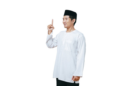 Young Muslim man in white baju kurung and black peci pointing one index finger upward against white background