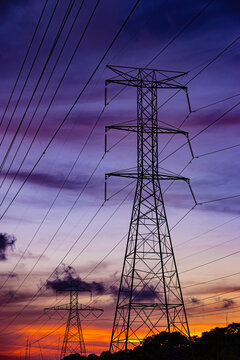 High voltage power lines and transmission towers silhouetted against a dramatic sunset sky.