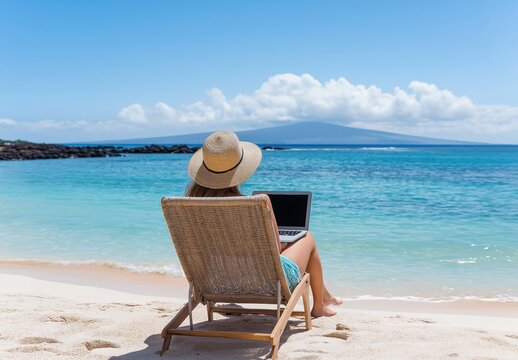 Woman in a straw hat sitting in a beach chair, using her laptop on a tropical beach with clear blue water