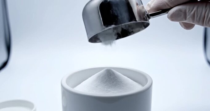 Hand pouring white powder into a white cup in a clean laboratory setting, emphasizing precision