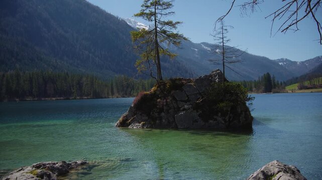 Crystal clear water ripples around a stone island at Hintersee, mountain lake nature perspective.