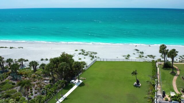 A vibrant green lawn adjacent to a turquoise ocean and sandy beach. Palm trees and natural landscaping enhance the coastal setting. Suitable for real estate and travel content.