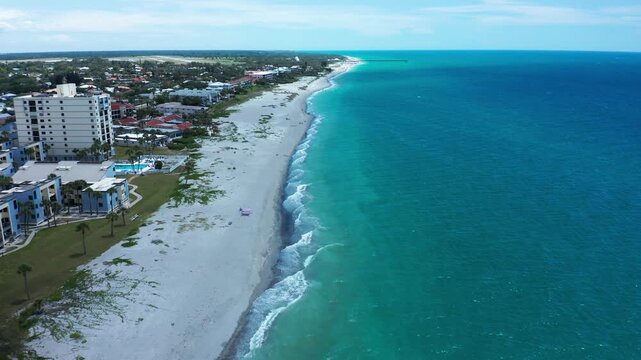 Aerial footage captures a stretch of sandy beach alongside residential buildings with vibrant turquoise waters. Ideal for travel promotions or real estate marketing.