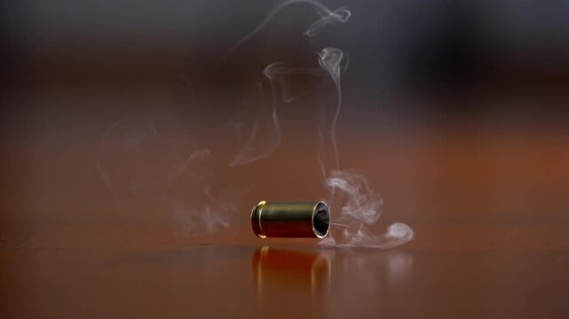 One bullet shell casing falling to wooden surface in slow motion. Fired brass casing bouncing after shot, close up action detail.