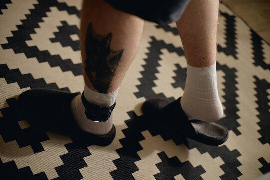 Close up of young adult man wearing electronic ankle monitor at home, standing under house arrest. Useful for legal restriction, criminal justice, surveillance, probation campaigns