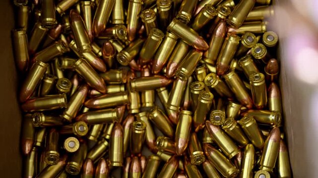 Bullets are falling from the persons hand to the box with ammunition. Close up of person sorting handgun cartridges on table.