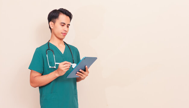 Smiling Southeast Asian male nurse or doctor in green scrubs holding a digital tablet. Professional healthcare worker presenting medical information or digital records on isolated background.