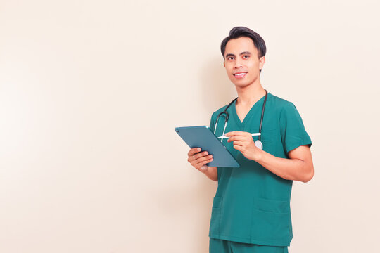 Smiling Southeast Asian male nurse or doctor in green scrubs holding a digital tablet. Professional healthcare worker presenting medical information or digital records on isolated background.